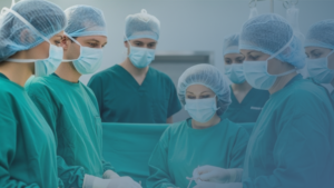 Equipe médica em centro cirúrgico realizando um procedimento, todos com roupas estéreis e máscaras.