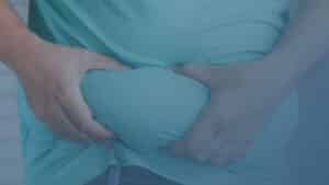 Pessoa apertando a região abdominal sobre a roupa, evidenciando excesso de gordura localizada.