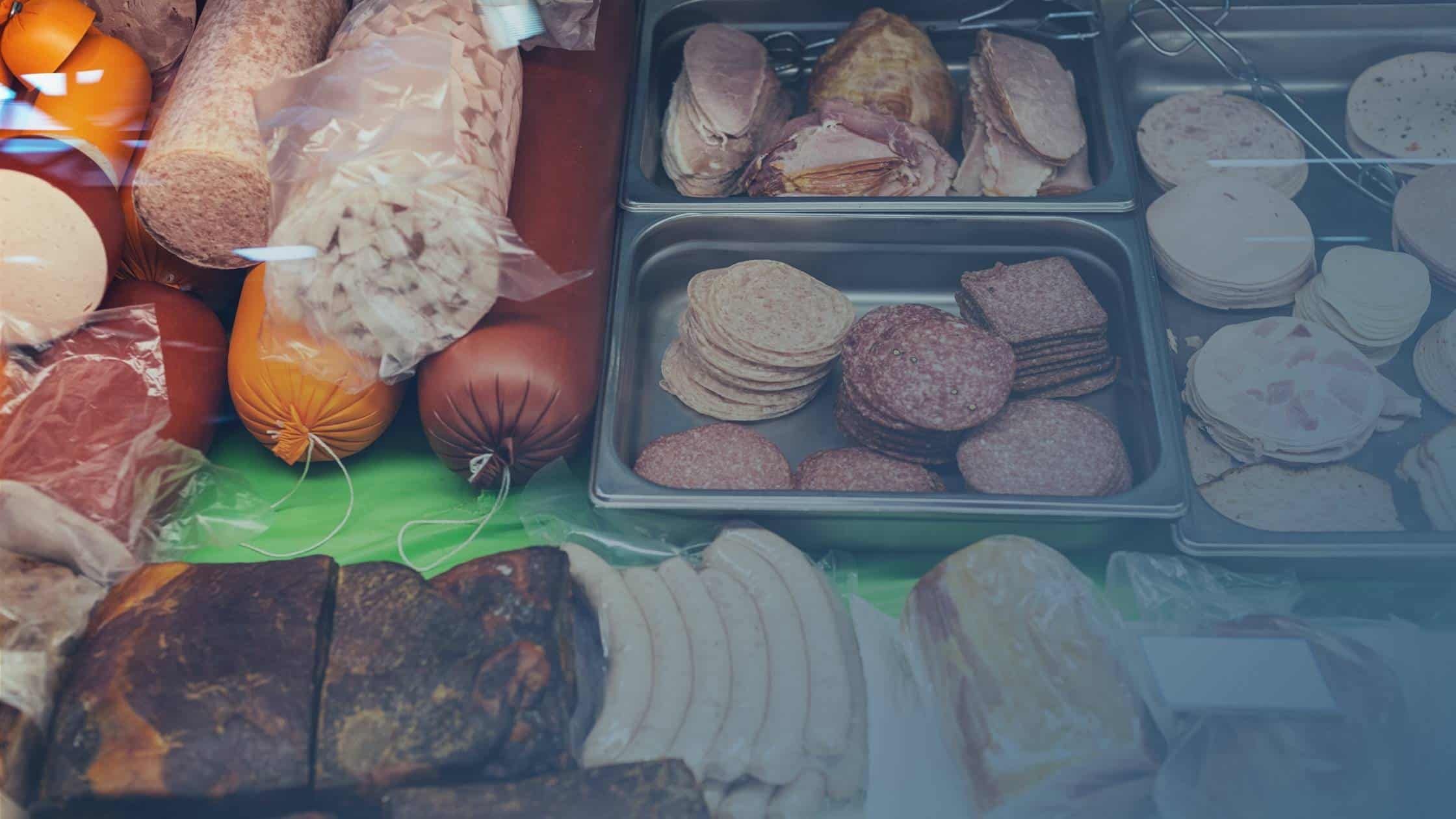Diversos tipos de embutidos e carnes ultraprocessadas expostos em balcão de mercado.