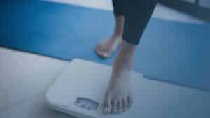 Pessoa subindo em uma balança, simbolizando a preocupação com o peso corporal e o processo de emagrecimento.