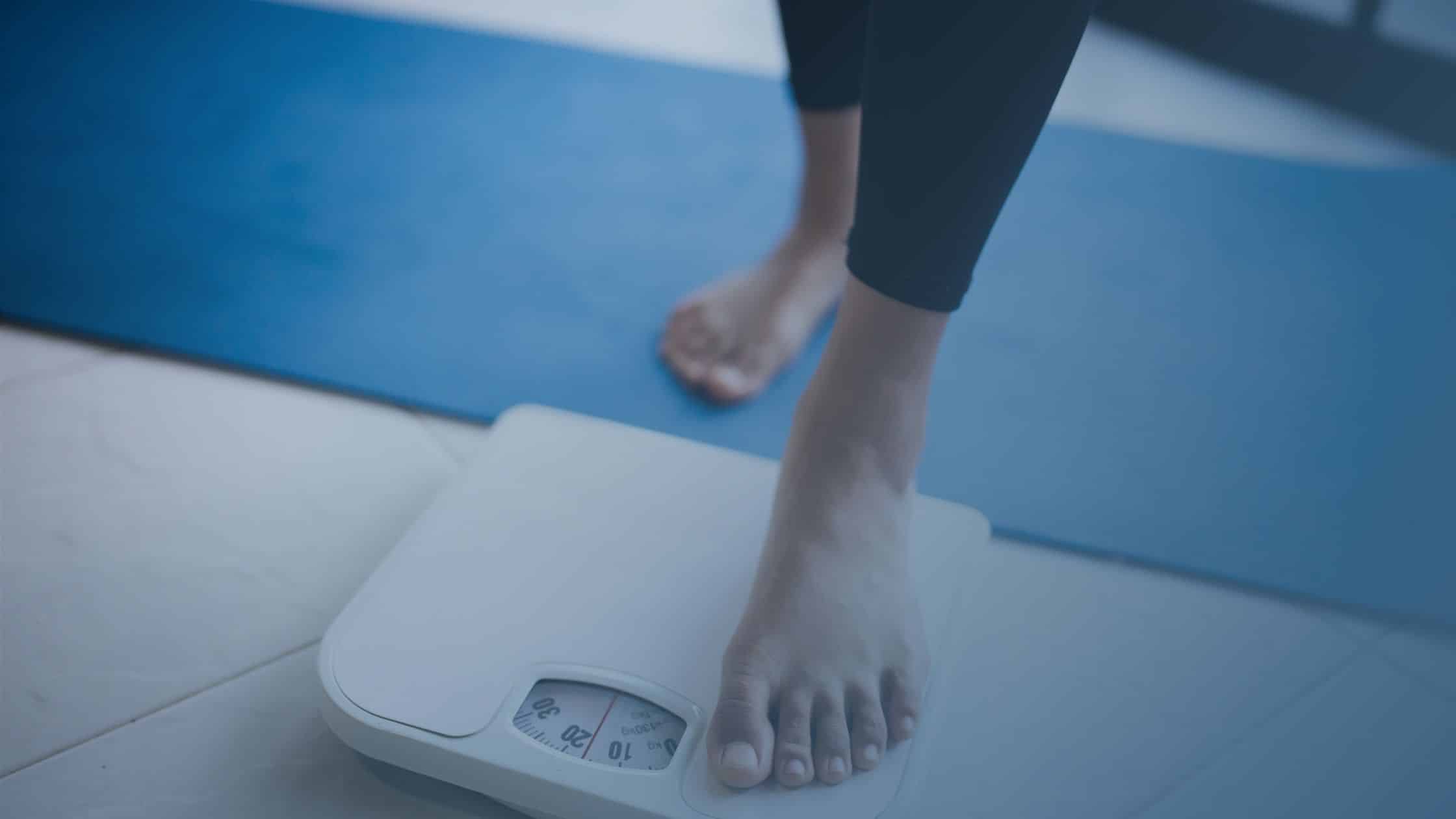 Pessoa subindo em uma balança, simbolizando a preocupação com o peso corporal e o processo de emagrecimento.