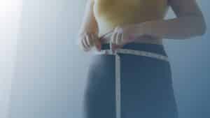 Pessoa medindo a circunferência abdominal com uma fita métrica, simbolizando o acompanhamento da perda de peso.